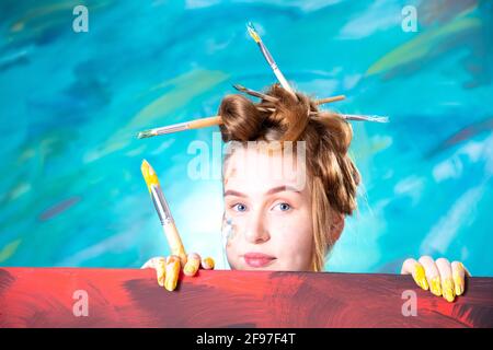 Junge Frau mit Updo und Pinsel in den Haaren beim Malen. Stockfoto