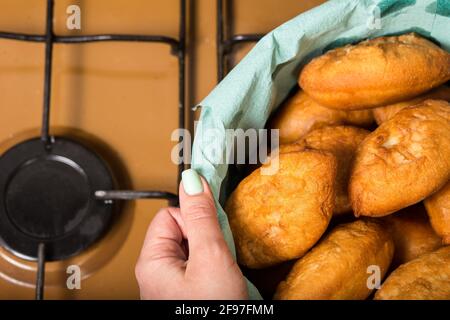 Weibliche Hände halten eine große Schüssel mit Pommes Frites mit Füllung auf einem Küchenherd. Stockfoto