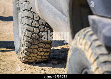 Geländereifen mit unebenem Profil für Geländefahrten auf unbefestigten Landstraßen, Nahaufnahme eines schmutzigen Autos, das mit Staub bedeckt ist. Stockfoto