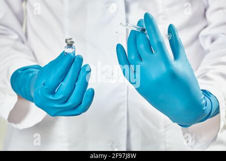 Arzt, der eine Spritze und ein Fläschchen mit einem Impfstoff hält In blauen Gummihandschuhen Stockfoto