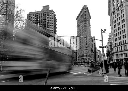 Flatiron Building in Midtown Manhattan an der Fifth Avenue in Long Exposition mit einem vorbeifahrenden Bus vor - klassische Straße Fotografieren mit einer Leica an einem kalten Wintertag In Manhattan Stockfoto