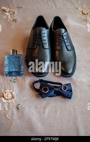 Accessoires für den Bräutigam. Schwarze Lederschuhe, goldene Eheringe, blaue Fliege, Parfüm Stockfoto