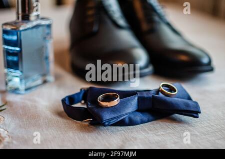 Accessoires für den Bräutigam. Schwarze Lederschuhe, goldene Eheringe, blaue Fliege, Parfüm Stockfoto