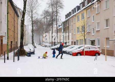 Essen, Nordrhein-Westfalen, Deutschland - Wintereinbruch im Ruhrgebiet, verschneite Wohnstraße in Holsterhausen, Mutter mit Kindern auf Schlitten auf der verschneiten Straße. Stockfoto