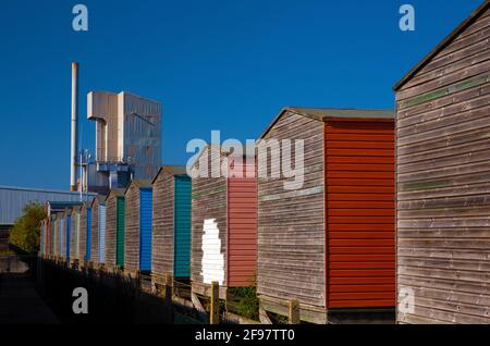 Die Brett-Aggregatfabrik überschattet traditionelle Strandhütten in Whitstable, Kent, Großbritannien. Stockfoto