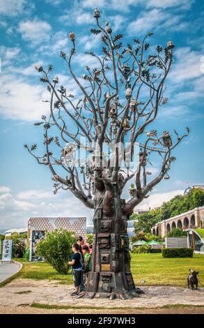 07-15-2019 Tiflis Georgien - Öffentlicher Park mit Sulpture Baum mit Viele Vogelhäuser und Georgia Capitol mit Flagge und Brücke in Hintergrund plus Hund stat Stockfoto