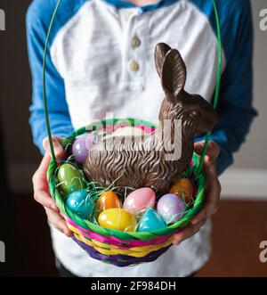 Nahaufnahme der Hände des Kindes, die einen Osterkorb voller Leckereien halten. Stockfoto