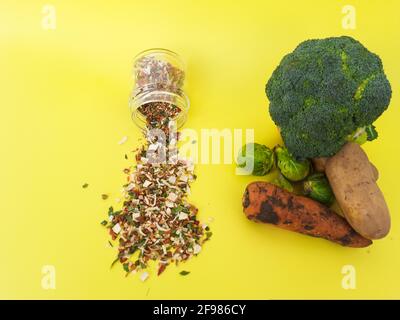 Getrocknete Würze aus dem Glas auf gelbem Hintergrund & roh gegossen Gemüse Stockfoto