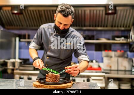 Fabelhafter Küchenchef, der Kräuter auf sein Fleisch legt Stockfoto