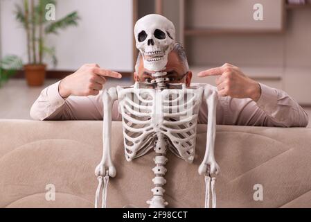 Alter Mann sitzt auf dem Sofa mit dem weiblichen Skelett In unsterbst Liebe Konzept Stockfoto