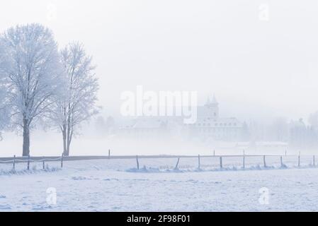 Ein magischer Wintermorgen im Kloster Schlehdorf am Kochelsee, Bayern, mit Frost, Sonnenschein, Nebel und frisch gefallener Schneedecke. Stockfoto