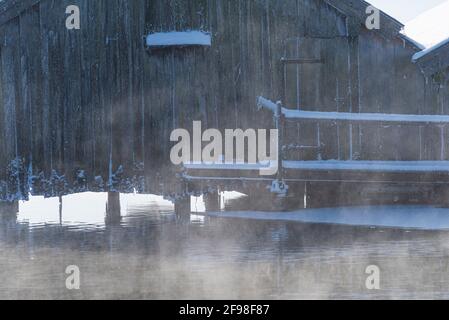 Ein magischer Wintermorgen in den Bootshäusern in Schlehdorf am Kochelsee, Bayern, mit Frost, Sonnenschein, Nebel und frisch gefallener Schneedecke. Nahaufnahme eines der 3 Bootshäuser. Stockfoto