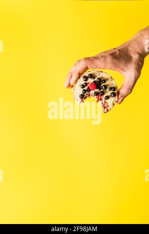 Hand halten knusprig aufgeblasen Reiskuchen mit frischen Früchten Blaubeeren Himbeeren vor dem gelben Hintergrund - gesund Bio-Vegetarier oder ve Stockfoto