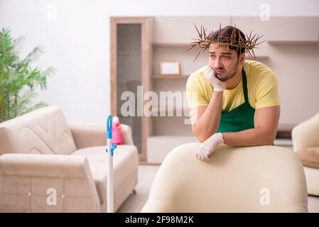 Junger männlicher Auftragnehmer, der auf dem Kopf einen stacheligen Kranz trägt und Hausarbeit leistet Stockfoto