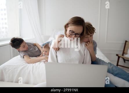 Beschäftigt kaukasische Frau versucht zu arbeiten, während Baby sitzen drei Kinder. Kaukasische alleinerziehende Mutter arbeitet von zu Hause aus mit den Kindern. Stockfoto