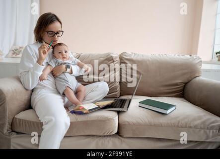 Beschäftigt kaukasische Frau versucht zu arbeiten, während Baby sitzen drei Kinder. Kaukasische alleinerziehende Mutter arbeitet von zu Hause aus mit den Kindern. Stockfoto