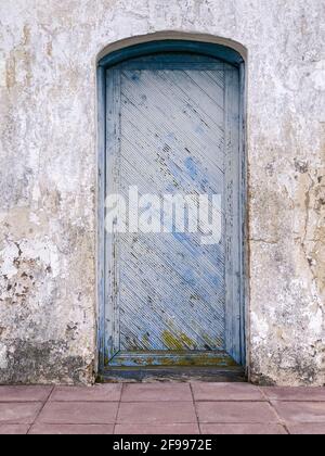 Holztür mit abblätternder blauer Farbstruktur auf grauem Stuck Wand Stockfoto