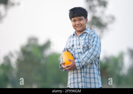 Ein Junge mit einer Melone im Feld Qualitätsauswahl für Verbraucher, Kid Lächeln mit Melone auf dem Bauernhof Stockfoto