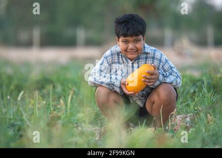 Ein Junge mit einer Melone im Feld Qualitätsauswahl für Verbraucher, Kid Lächeln mit Melone auf dem Bauernhof Stockfoto