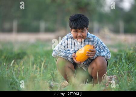 Ein Junge mit einer Melone im Feld Qualitätsauswahl für Verbraucher, Kid Lächeln mit Melone auf dem Bauernhof Stockfoto