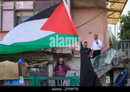 Palästinenser und israelische linke Aktivisten halten die palästinensische Fahne vor einem Haus hoch, das von jüdischen Siedlern während einer Demonstration gegen Siedlungsaktivitäten in Scheich Jarrah, einem überwiegend palästinensischen Viertel, am 16. April 2021 in Ostjerusalem, Israel, besetzt wurde. Das palästinensische Viertel Sheikh Jarrah ist derzeit das Zentrum einer Reihe von Eigentumsstreitigkeiten zwischen Palästinensern und Israelis. Einige Häuser wurden nach einem Gerichtsurteil von israelischen Siedlern besetzt. Stockfoto