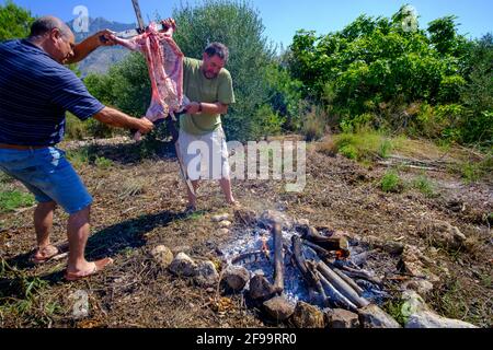 In Altea La Vella, Alicante, Spanien, grillen zwei Männer auf einem Eisenkreuz neben dem offenen Feuer Stockfoto