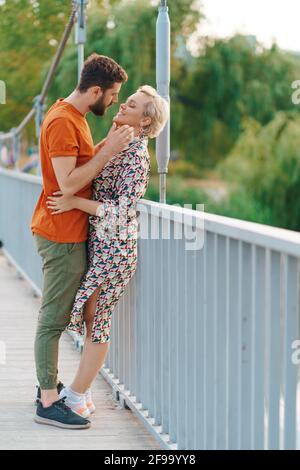 Glücklich lächelndes junges Paar umarmt und küsst auf Brücke Stockfoto