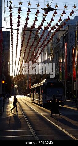 Abendszene in der Innenstadt von Melbourne während der goldenen Stunde vor Sonnenuntergang mit Zwei Frauen überqueren die Straße vor einer Straßenbahn Straßenbahn-Seilbahn Stockfoto