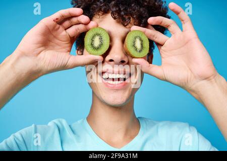 Mann mit lockigem Haar, der Kiwi in der Nähe des Klassengesichts hält Emotionen Stockfoto