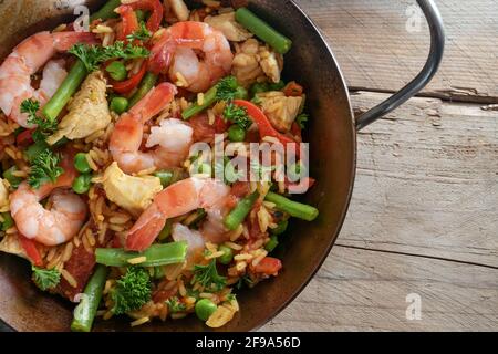 Hausgemachte spanische Paella, Reisgericht mit Meeresfrüchten, Huhn und Gemüse in einer Pfanne auf einem rustikalen Holztisch, Nahaufnahme, hoher Engel Blick von oben Stockfoto
