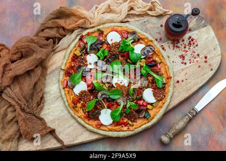 Draufsicht auf rohe vegane Pizza neben einer alten Rote Pfeffermühle mit getrockneten Pfefferkörnern auf einem Holzbrett Stockfoto