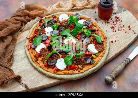 Nahaufnahme einer rohen veganen Pizza neben einer alten Pfeffermühle mit getrockneten Pfefferkörnern auf einem Holzbrett Stockfoto