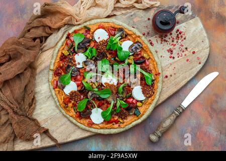 Draufsicht auf rohe vegane Pizza neben einer alten Rote Pfeffermühle mit getrockneten Pfefferkörnern auf einem Holzbrett Stockfoto