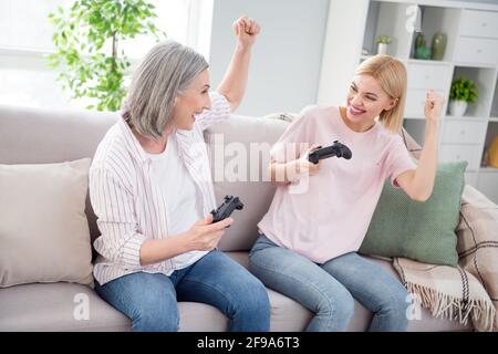 Foto von fröhlich glücklich grauhaarigen blonden Frauen sitzen Sofa Win Spiel halten Joystick drinnen im Haus Stockfoto