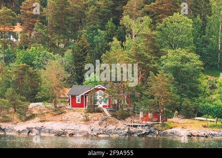 Schweden. Wunderschöne Red ASwedish Holzhütten Häuser an der Rocky Island Küste im Sommer. See- Oder Flusslandschaft Stockfoto