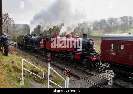 Historische Dampfzüge (Loks), die Rauchwolken schwappen, stoppten bei der Überfahrt (Mann, der auf dem Gleis fotografiert) - Heritage Railway, KWVR, Yorkshire, England, Großbritannien.