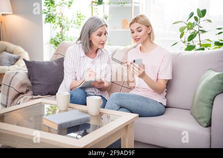 Foto von zwei Personen, die auf der Couch sitzen, sehen aufmerksam Telefon Handflächen mit Schreibanweisungen notieren sich Notizen im Innenbereich Stockfoto