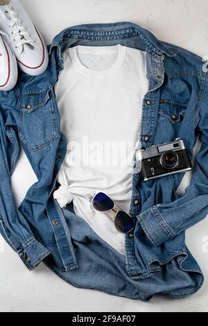 Weißes T-Shirt mit Platz für Text. Blaues Jeanshemd, Turnschuhe, Brille - ein Satz von Kleidung zum Wandern. T-Shirt-Modell zum Drucken. Stylisches Set Stockfoto