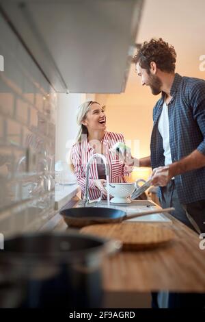 Bild eines jungen kaukasischen erwachsenen Paares, das beim Waschen Spaß hat Geschirr Stockfoto