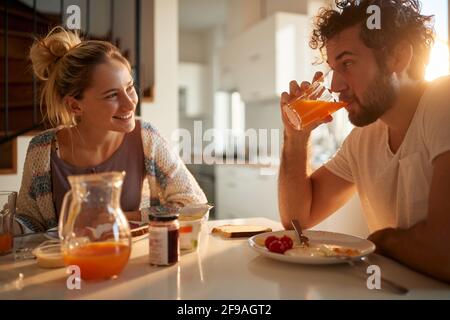 Das junge kaukasische Paar frühstückte im sonnigen Speisesaal und schaute sich lächelnd an Stockfoto