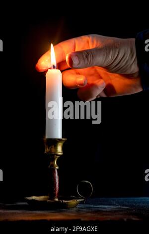 Ein Mann stellt mit Daumen und Zeigefinger eine Kerze aus. Stockfoto