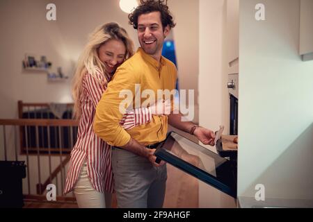 Junge Erwachsene kaukasische Frau umarmt ihren Mann, der kocht. valentine, romantisch, Zweisamkeit Stockfoto
