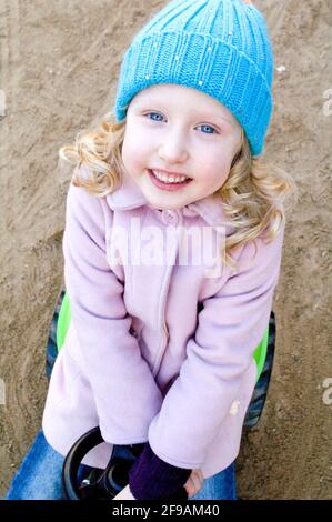 Kleinkind sitzt auf Spielzeugauto und lächelt, blonde Mädchen, Porträt-Format, Serie von Porträts Stockfoto