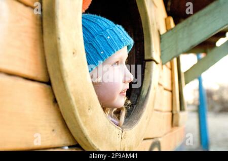 Kleinkind auf dem Spielplatz sieht nachdenklich aus dem Fenster, blonde Mädchen, Serie von Porträts Stockfoto