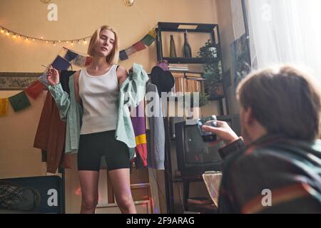 Junge Frau, die eine Zigarette raucht und mit einem jungen Mann tanzt Sitzen und Wein trinken während der Retro-Party zu Hause Stockfoto