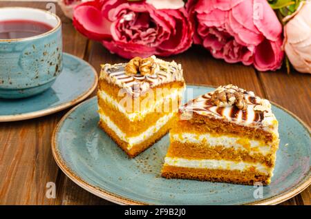 Zwei Stücke Karottenkuchen auf blauem Teller, eine Tasse Tee auf einem Holztisch. Studio Photo Stockfoto