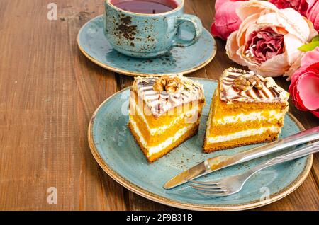 Zwei Stücke Karottenkuchen auf blauem Teller, eine Tasse Tee auf einem Holztisch. Studio Photo Stockfoto