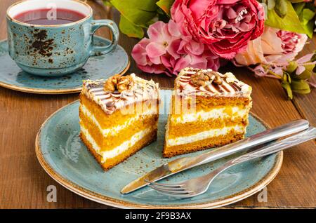 Zwei Stücke Karottenkuchen auf blauem Teller, eine Tasse Tee auf einem Holztisch. Studio Photo Stockfoto