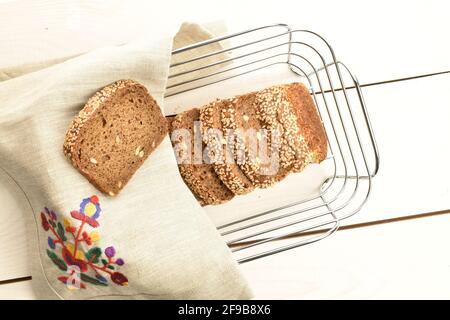 Mehrere Stücke von frisch duftendem, schmackhaftem Sesambrot in einem Korbkorb aus Metallstäben mit Leinenserviette, Nahaufnahme, auf einem Tisch aus Holz. Stockfoto
