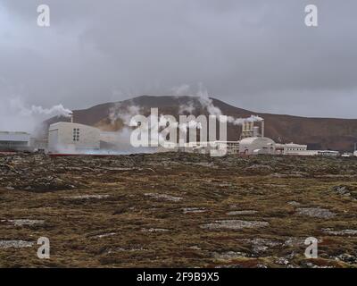 Blick auf das dampfende geothermische Kraftwerk Svartsengi bei Grindavik, Halbinsel Reykjanes, Island mit moosbedecktem Lavafeld im Winter davor. Stockfoto